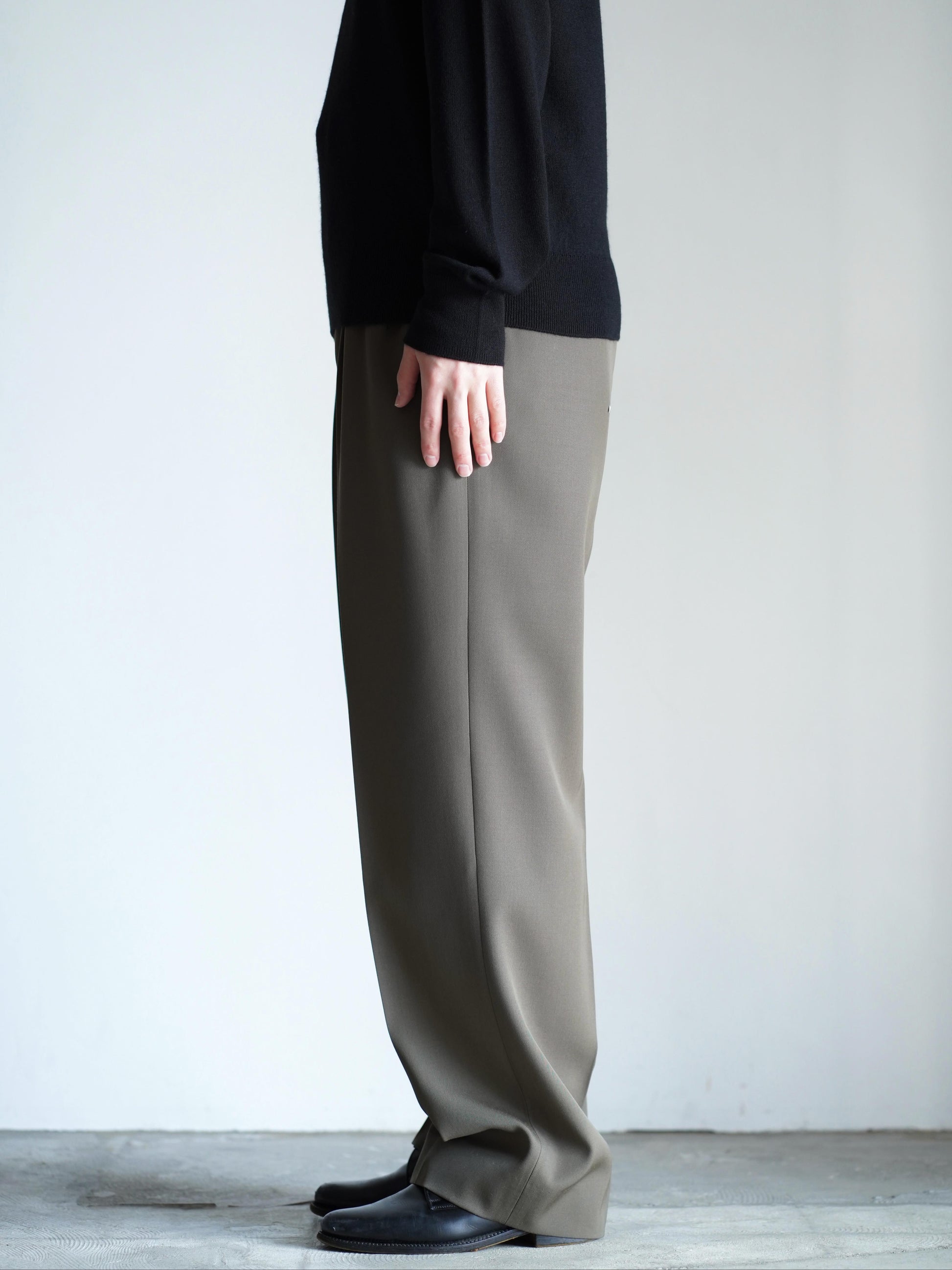 AURALEEのLIGHT WOOL MAX GABARDINE TWO-TUCK SLACKSのカラーはダークオリーブブラウンの横向きの着用画像です。