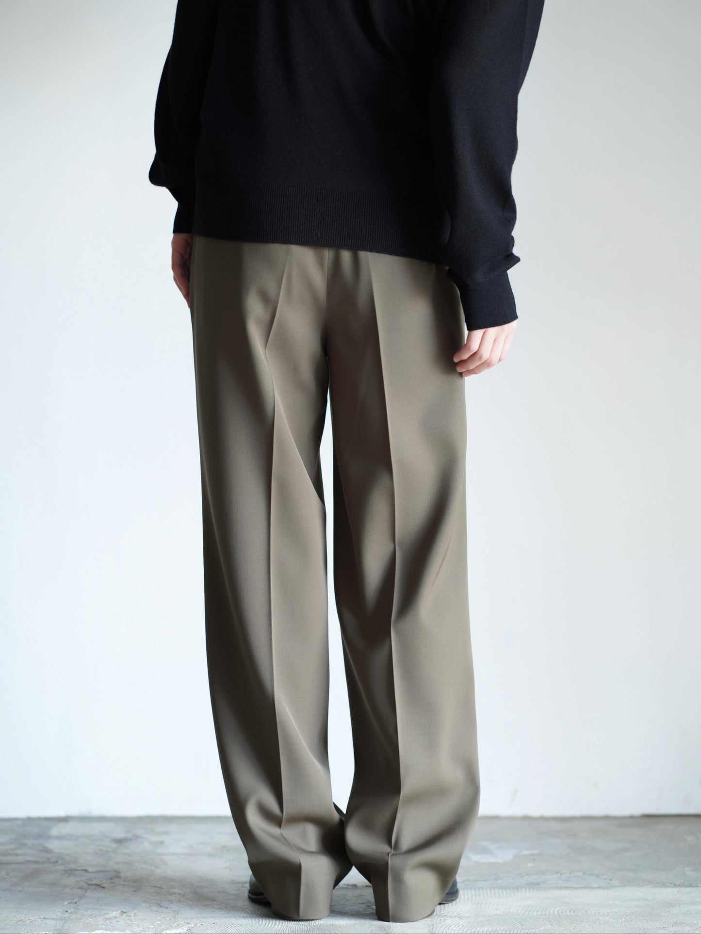 AURALEEのLIGHT WOOL MAX GABARDINE TWO-TUCK SLACKSのカラーはダークオリーブブラウンの後ろ向きの着用画像です。