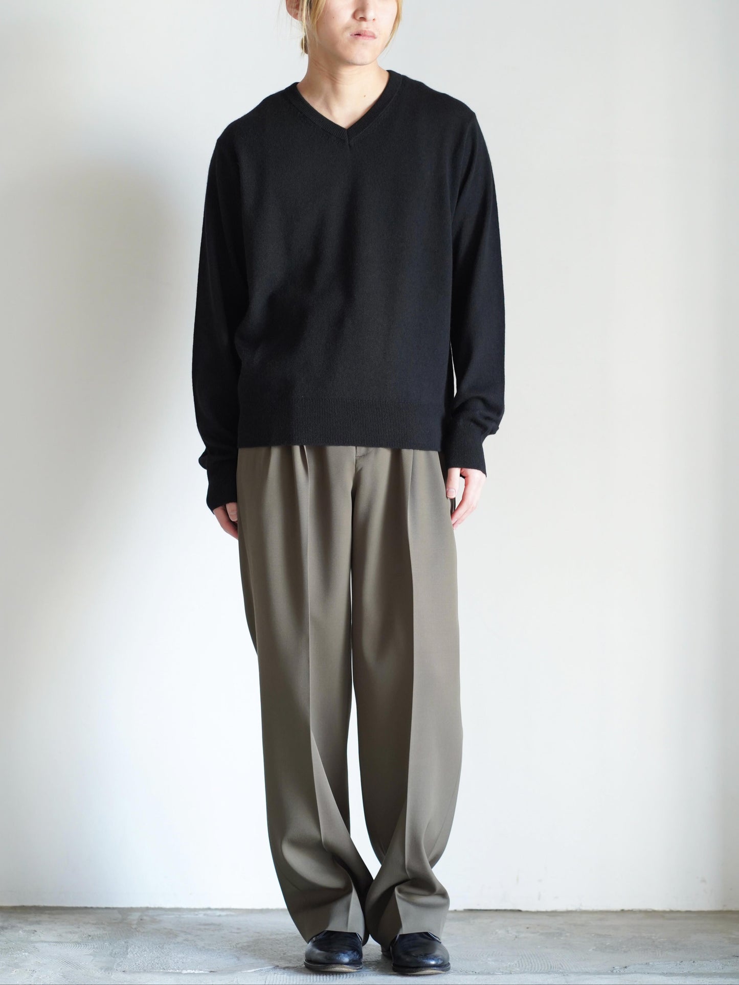 AURALEEのLIGHT WOOL MAX GABARDINE TWO-TUCK SLACKSのカラーはダークオリーブブラウンとAURALEEのSUPER FINE CASHMERE SILK KNIT V-NECK P/Oのカラーはブラックを着用した全体が写った着用画像です。