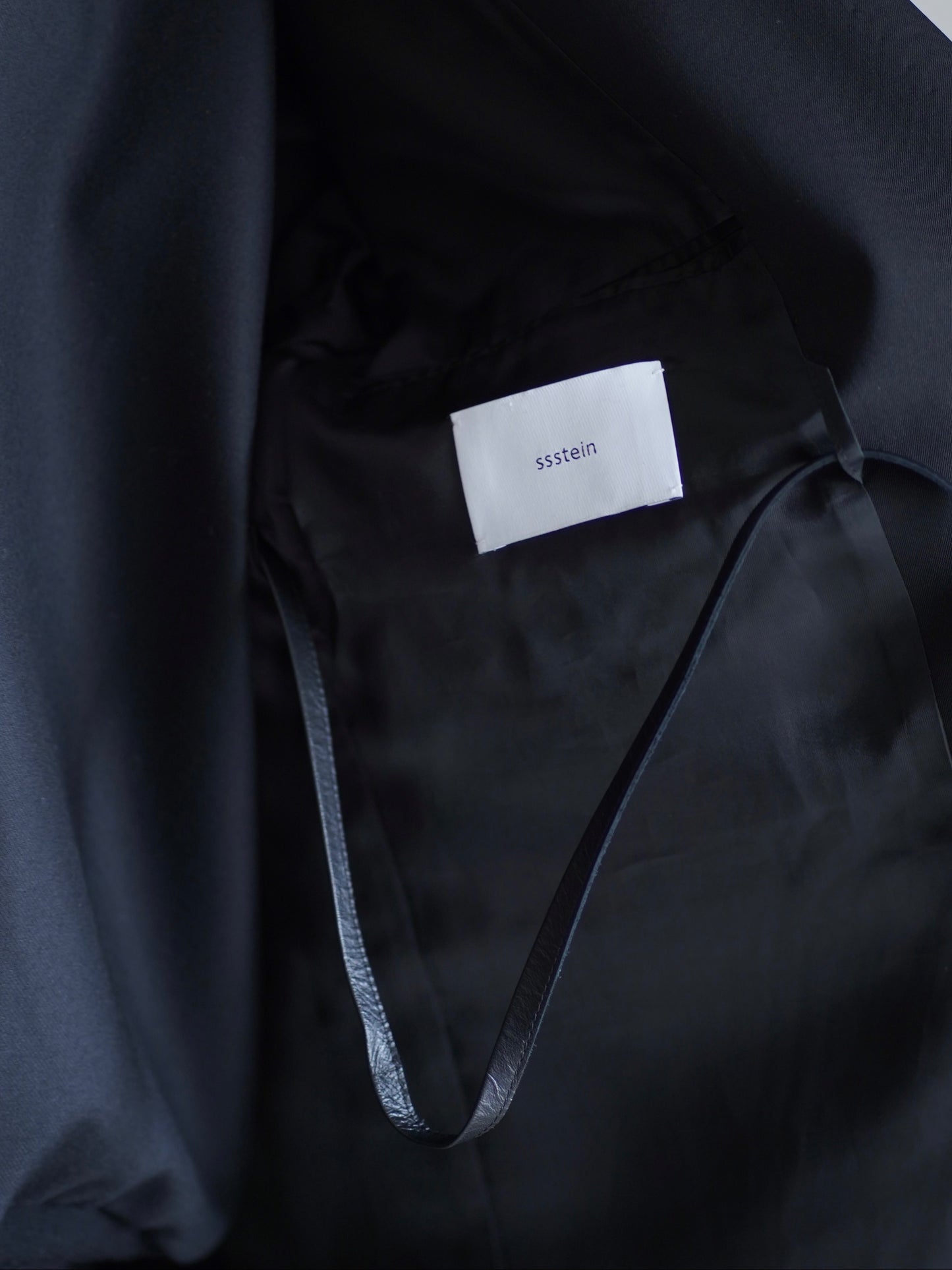 sssteinのOVERSIZED SINGLE BREASTED LONG JACKETのカラーはBLACKの左胸のジャケットの内側のブランドロゴとレザーコードを収納した際の画像です。こちらの商品は通販での購入が可能です。