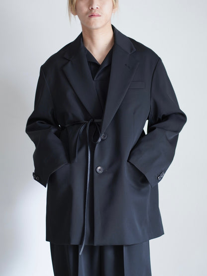 sssteinのOVERSIZED SINGLE BREASTED LONG JACKETのカラーはBLACKで、レザーコードでウエストを結んだトップスの着用画像です。こちらの商品は通販での購入が可能です。