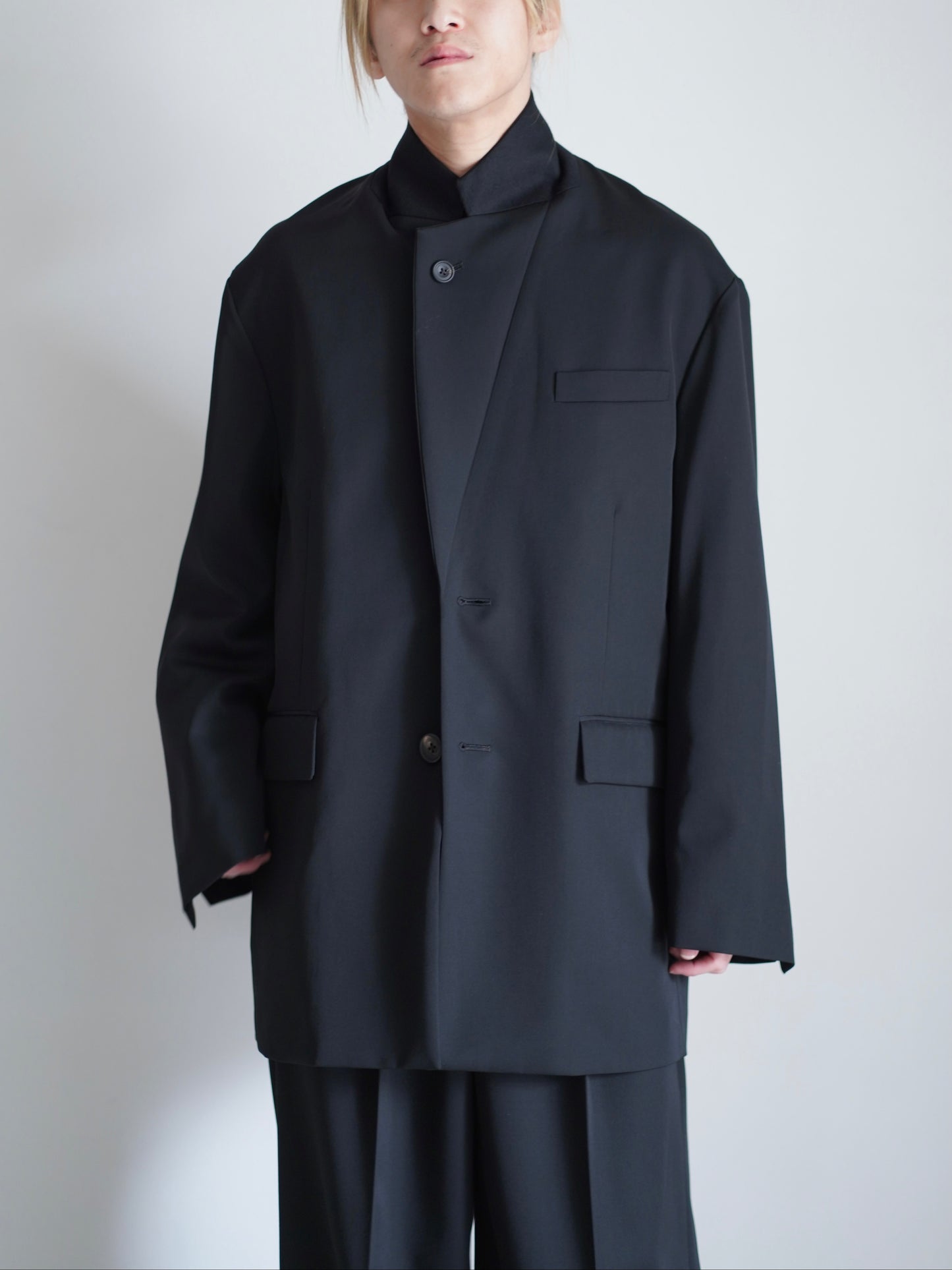 sssteinのOVERSIZED SINGLE BREASTED LONG JACKETのカラーはBLACKのラペルを立てて着用しているトップスの着用画像です。こちらの商品は通販での購入が可能です。