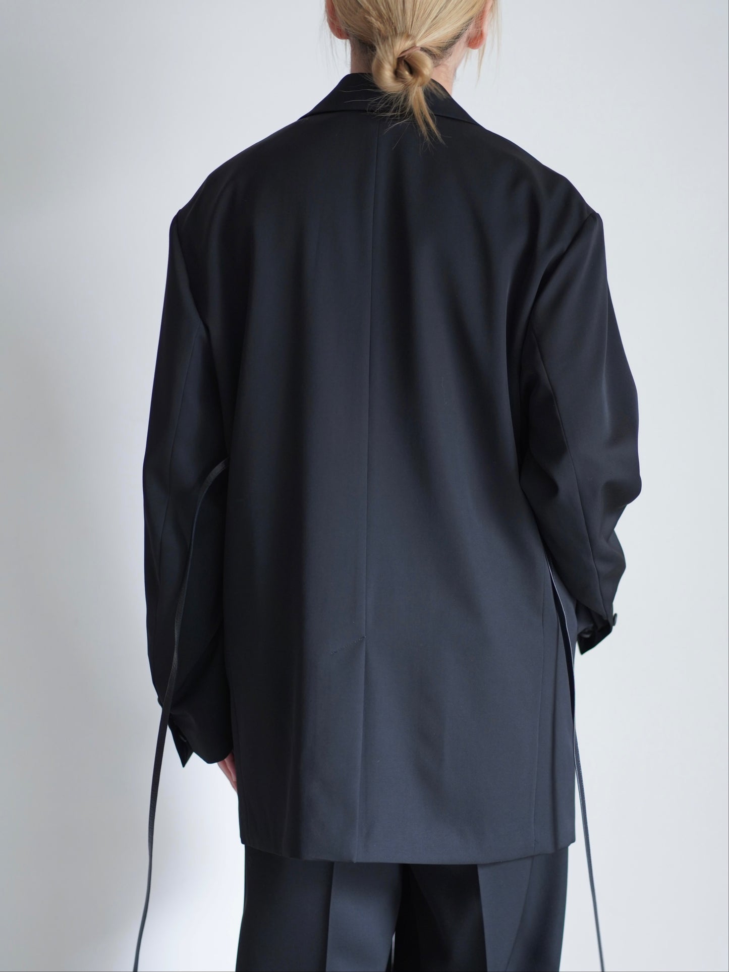 sssteinのOVERSIZED SINGLE BREASTED LONG JACKETのカラーはBLACKのトップスの後向きの着用画像です。こちらの商品は通販での購入が可能です。