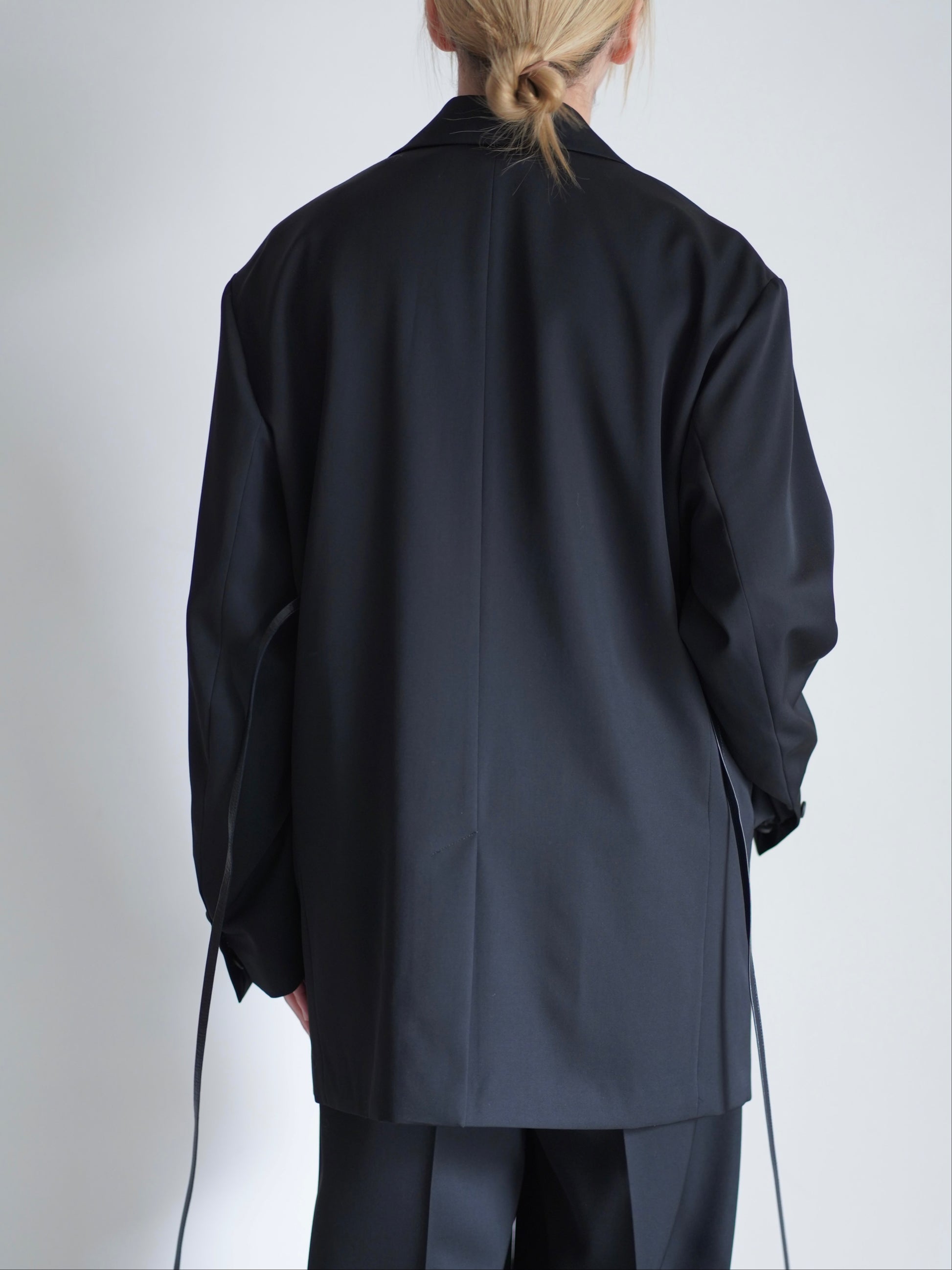 sssteinのOVERSIZED SINGLE BREASTED LONG JACKETのカラーはBLACKのトップスの後向きの着用画像です。こちらの商品は通販での購入が可能です。